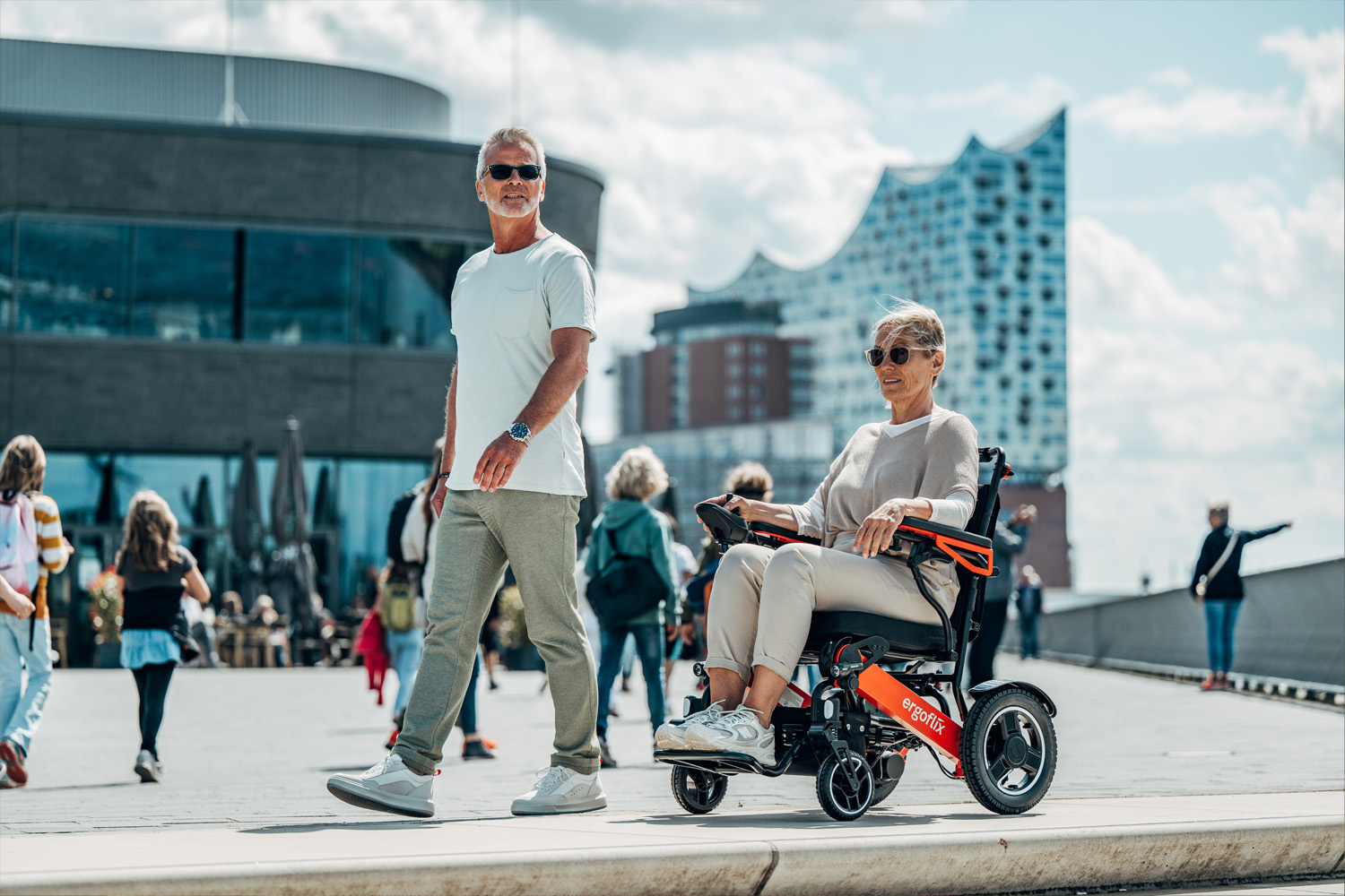 Das Bild zeigt eine Dame im Rollstuhl und einen Mann an der Promenade lang laufen.