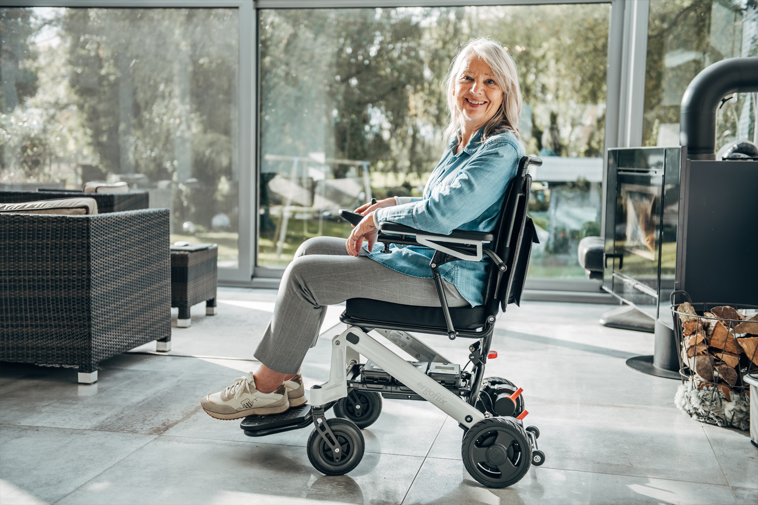 Auf dem Bild ist eine Frau im Rollstuhl zu sehen, sie steht seitlich zur Kamera und befindet sich in einem lichtdurchfluteten Raum.