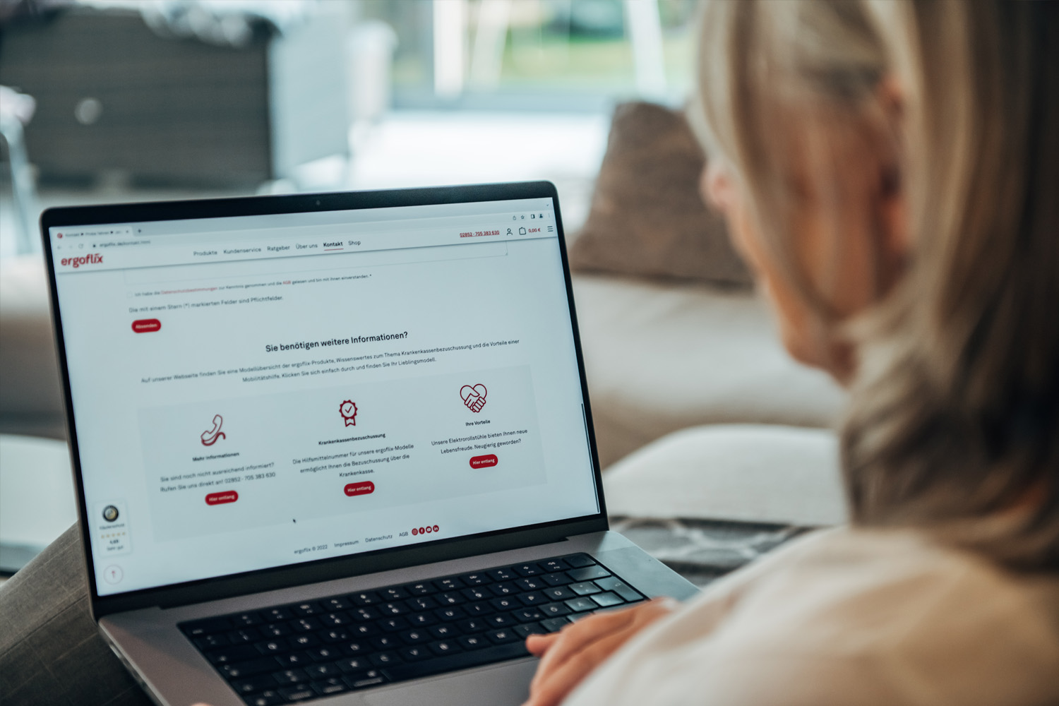 Das Bild zeigt einen Teil einer Frau von hinten mit Blick über ihre Schulter auf einen geöffneten Laptop.