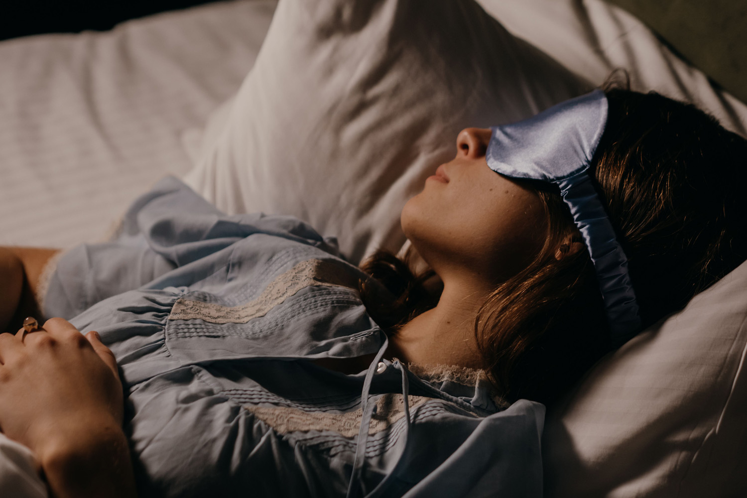 Das Bild zeigt eine Frau, die in einem abgedunkelten Raum mit Schlafmaske im Bett liegt.