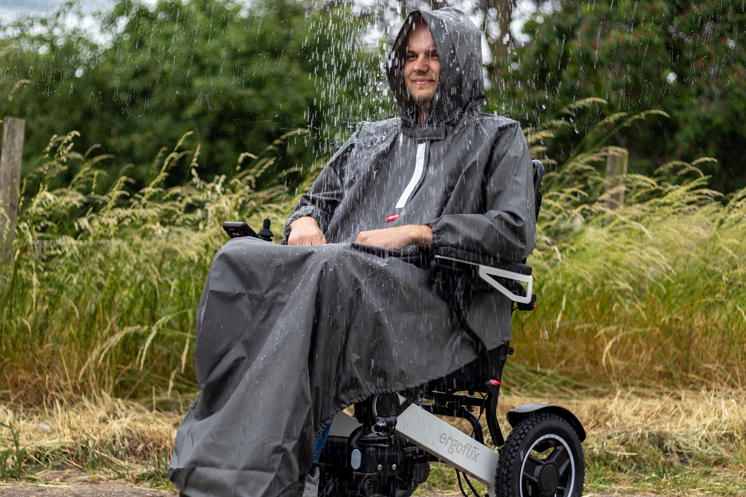 Das Bild zeigt einen Mann im Rollstuhl bei Regen, der ein Regencape trägt.