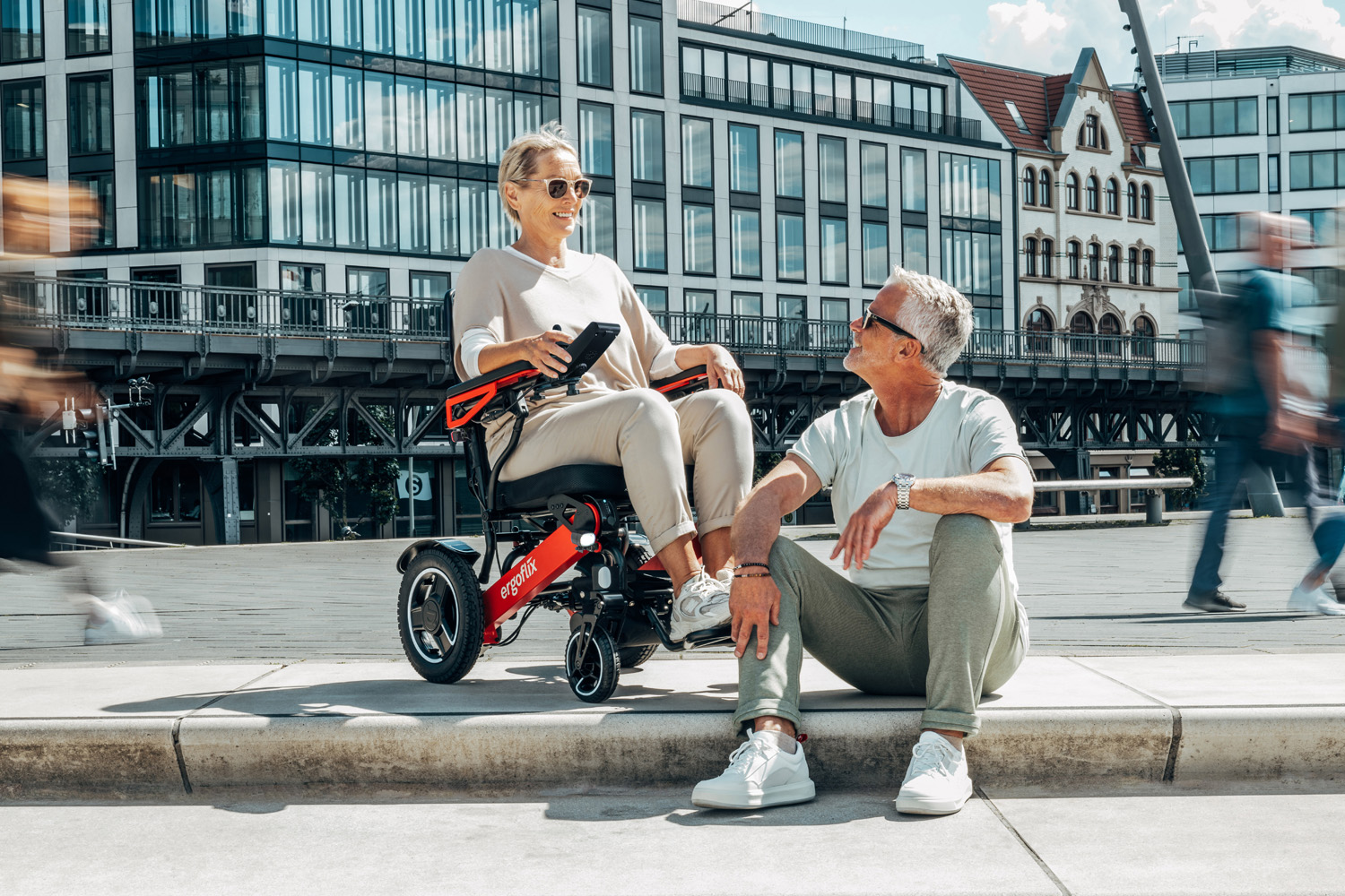 Das Bild zeigt eine Frau im Rollstuhl vor einer Stufe, ein Mann sitzt daneben auf der Stufe.