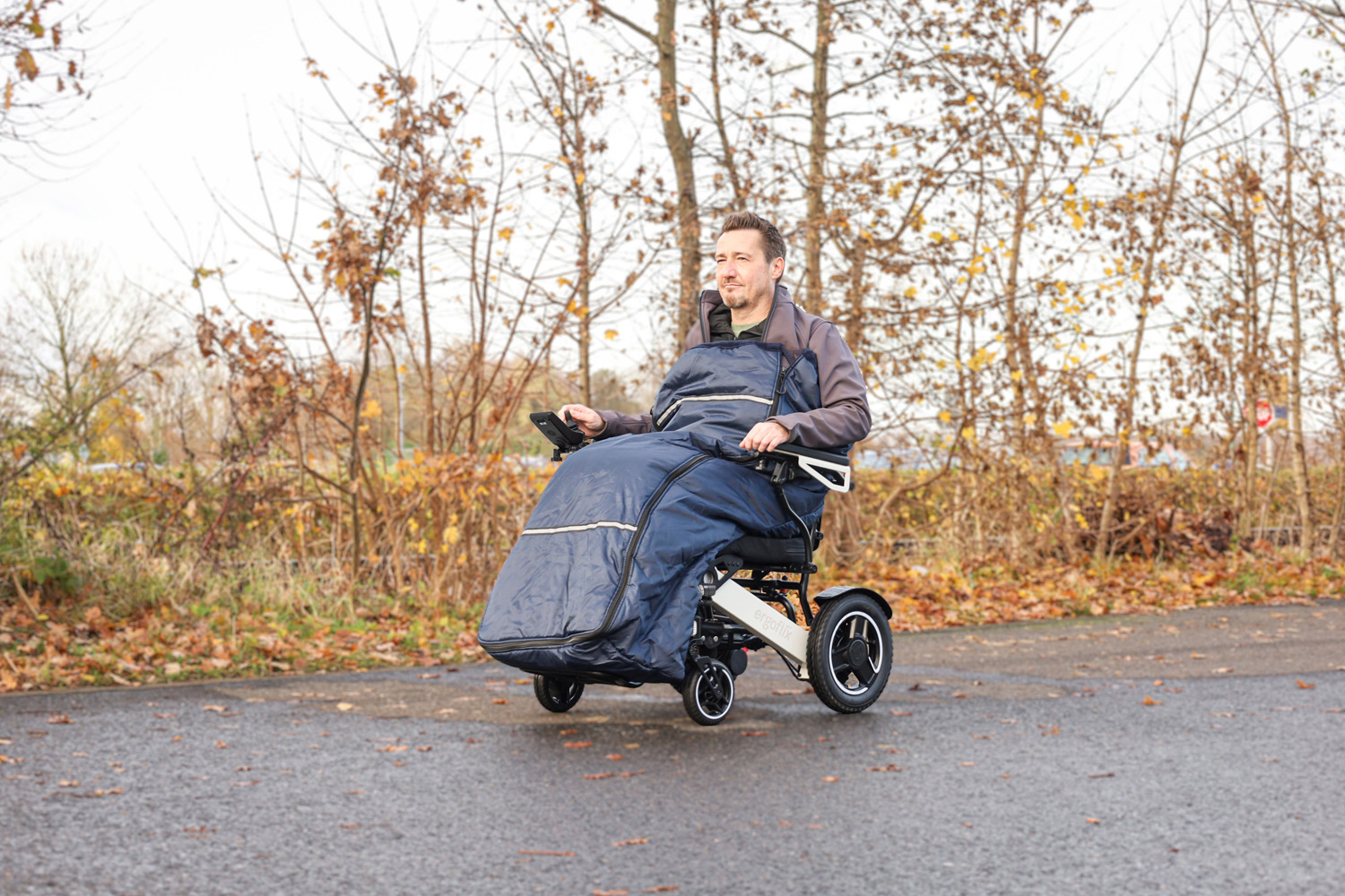 Das Bild zeigt einen Mann, der einen Schlupfsack nutzt und in einem Rollstuhl von ergoflix draußen fährt.