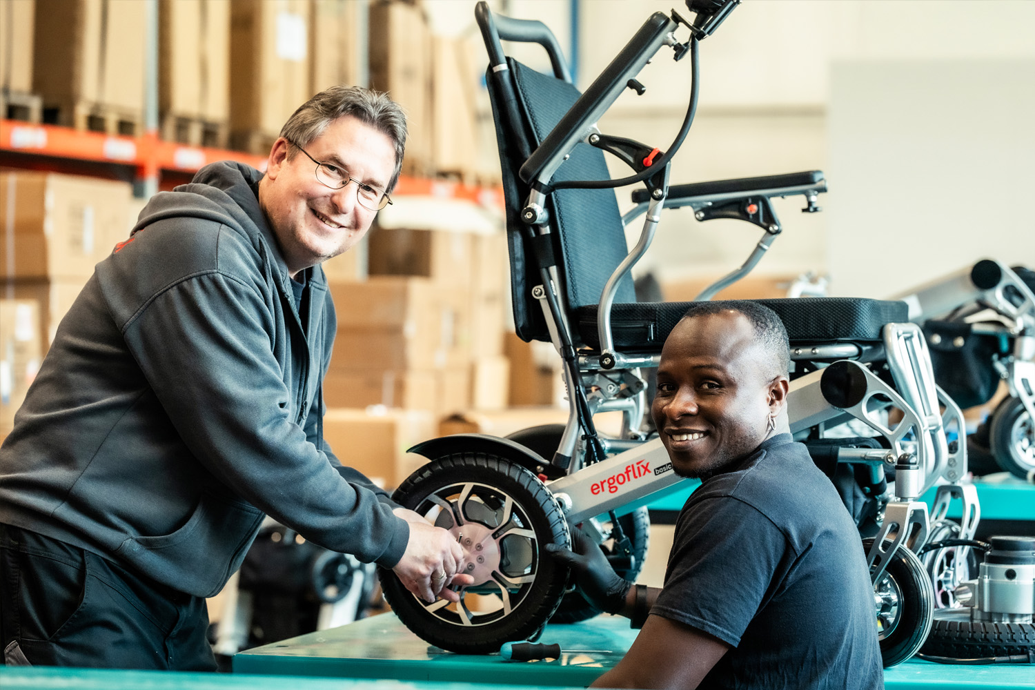 Auf dem Bild sind zwei Männer zu sehen, die einen Rollstuhl reparieren.