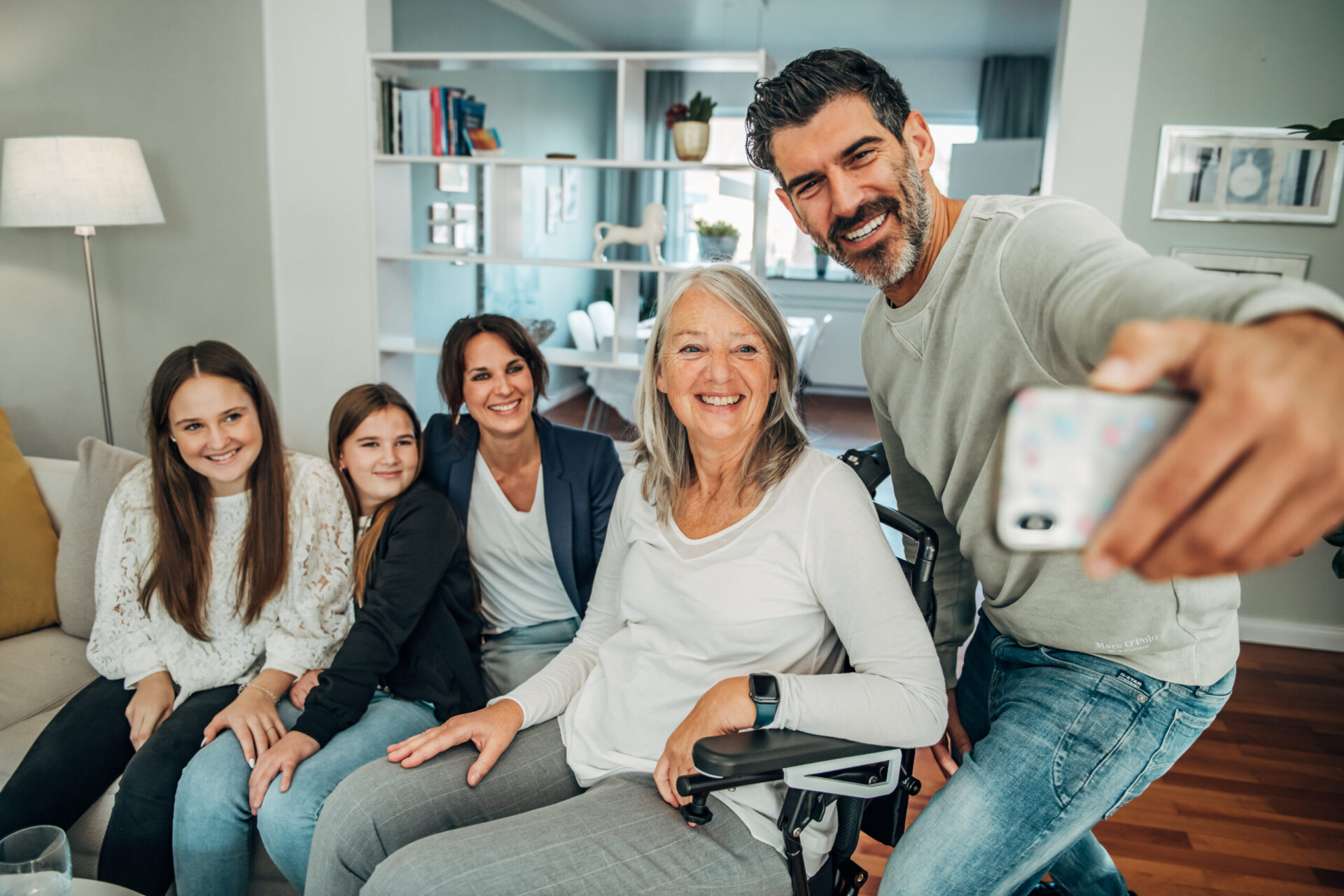 Dieses Bild zeiggt eine Oma, die im Indoor-Rollstuhl sitzt, mit ihrer Familie