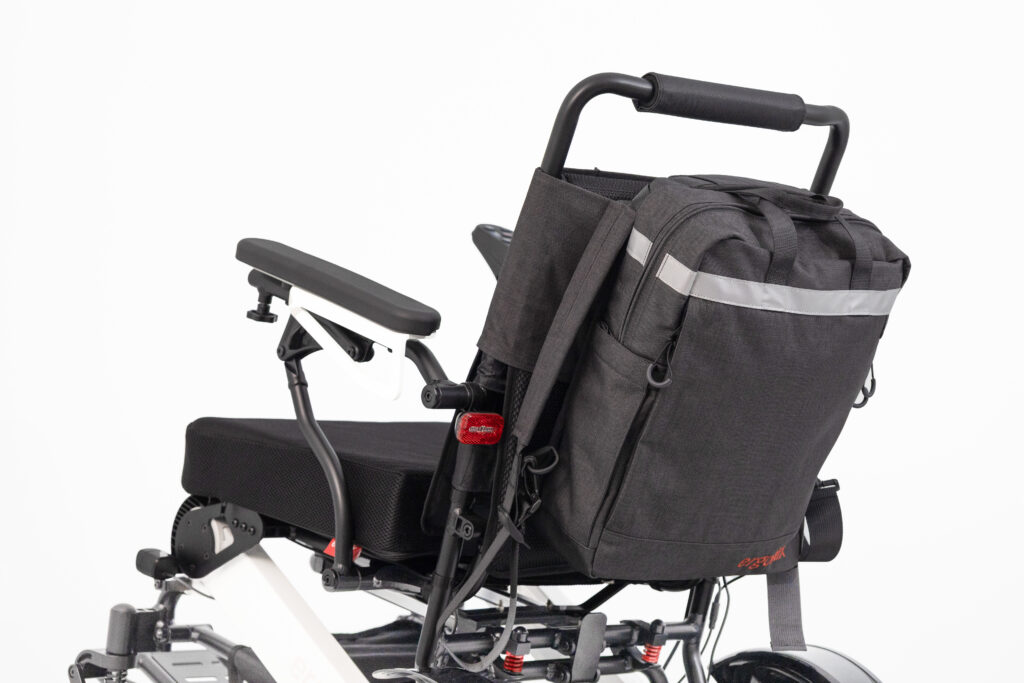 Das Bild zeigt einen Elektrorollstuhl von hinten, dort ist an der Rückenlehne ein Rucksack von ergoflix angebracht.
