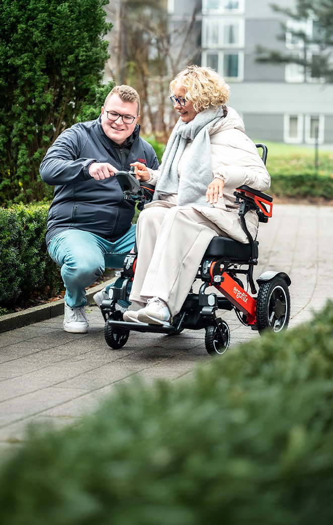 Ein junger Mitarbeiter der Firma ergoflix zeigt bei einer Probefahrt einer älteren Dame den roten ergoflix® LX in der Natur.