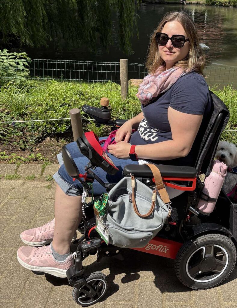 Das Bild zeigt eine Frau, die im Rollstuhl sitzt und damit in der Natur unterwegs ist.
