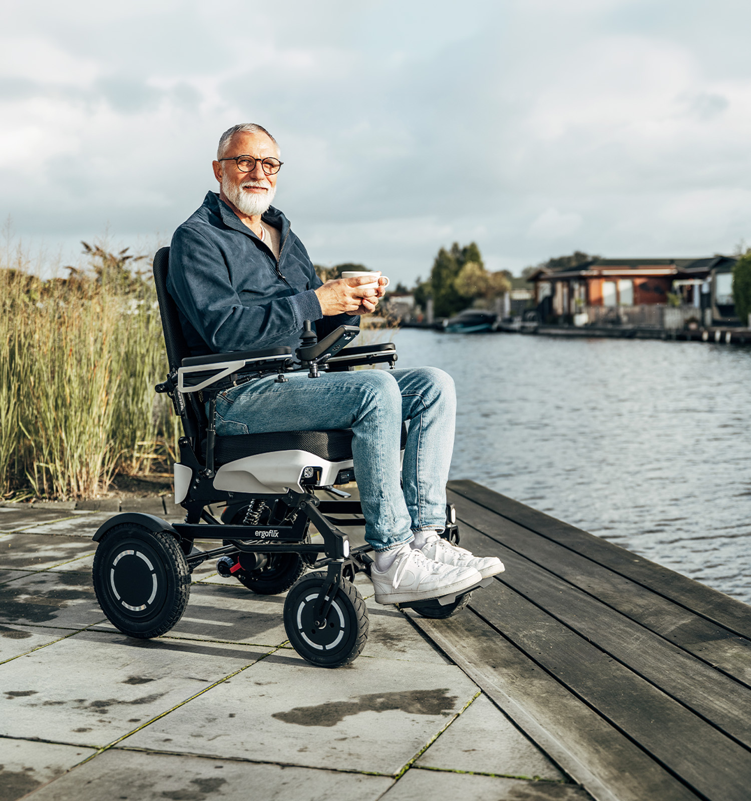 Man sitting in an ergoflix vario on a jetty by the water, holding a cup